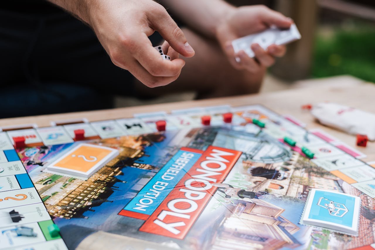 Crop anonymous male player with dices and fake money playing Monopoly at table with deed cards